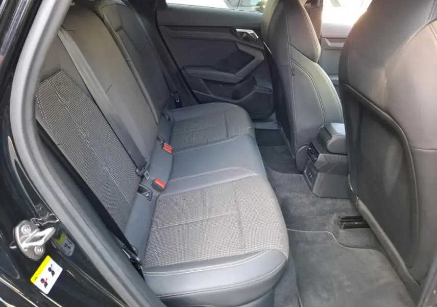 Vue intérieure arrière côté gauche de l'Audi A3 Sportback noire, montrant les sièges arrière en tissu et cuir avec ceintures rouges.