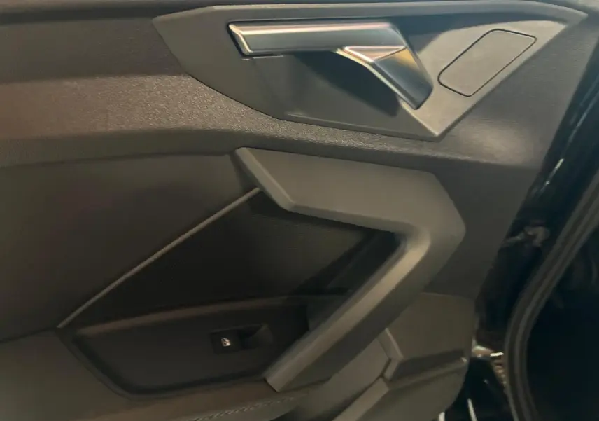 Gros plan sur la porte avant droite noire de l'Audi A3 Sportback 2023 avec accoudoir en similicuir et insert aluminium.