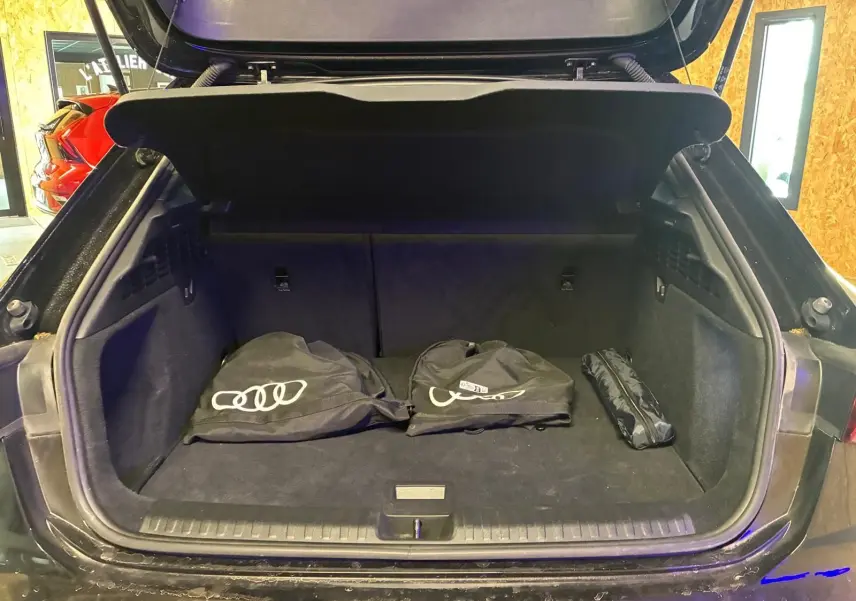 Coffre ouvert d’une Audi A3 Sportback noire, vue arrière, avec housses de protection Audi posées à l’intérieur.