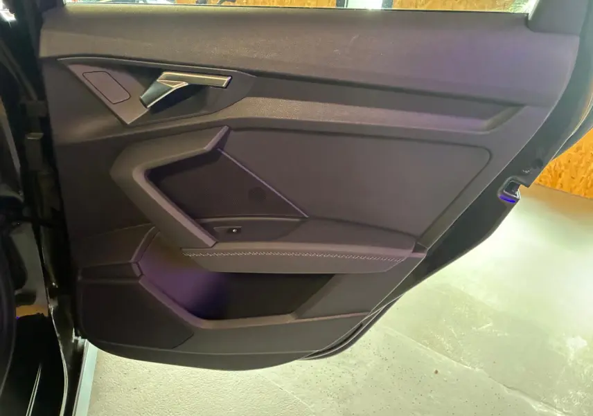 Vue rapprochée de la portière avant gauche noire de l'Audi A3 Sportback 2023 avec accoudoir en similicuir et insert aluminium.