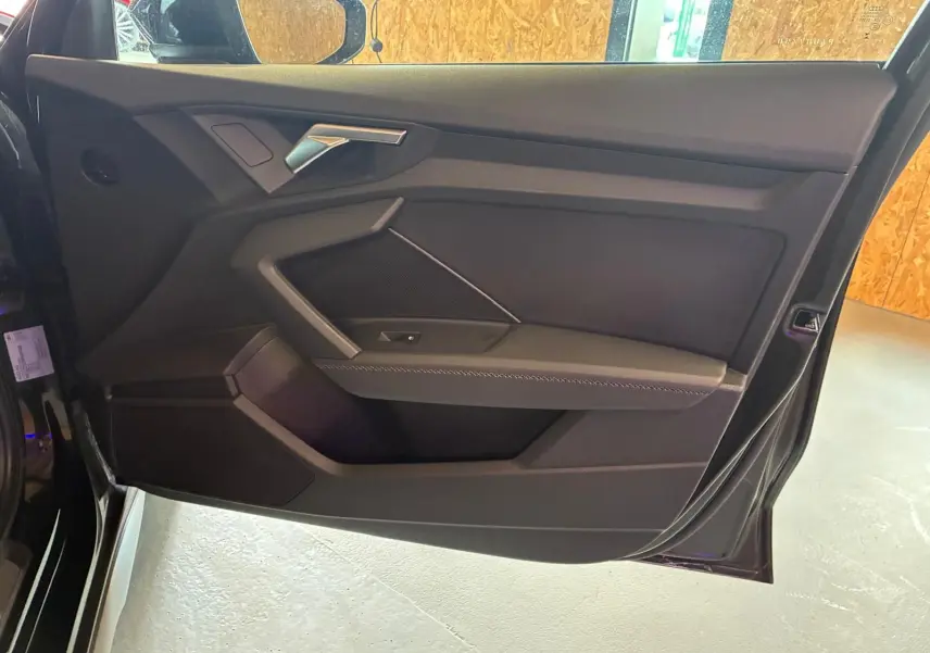 Vue rapprochée du panneau de porte côté gauche noir de l'Audi A3 Sportback 2023 avec accoudoir en similicuir et insert aluminium.