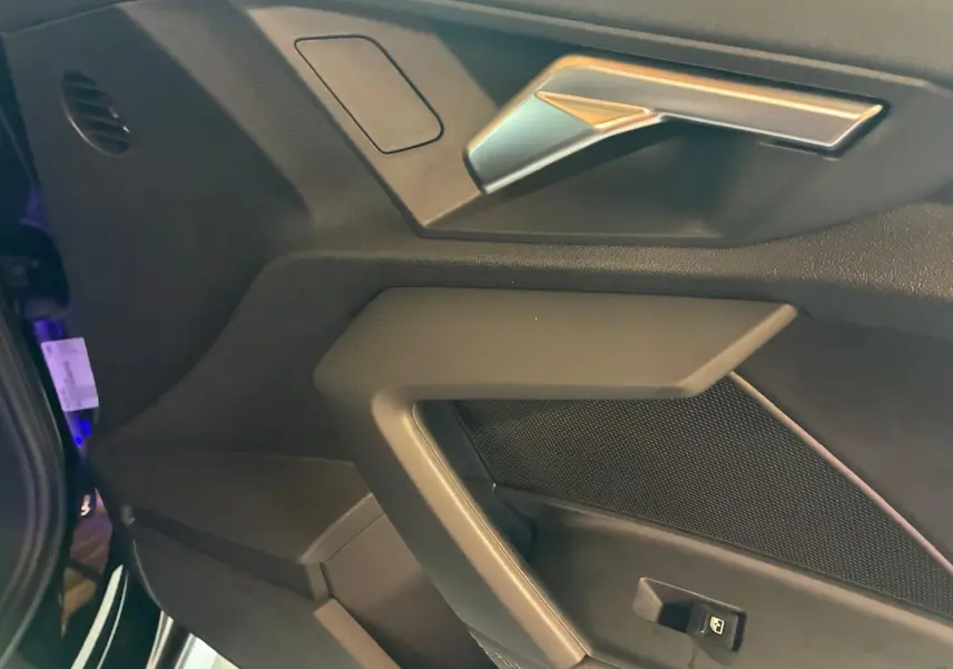 Détail de la portière côté gauche noire de l’Audi A3 Sportback 2023 avec poignée argentée et bouton de lève-vitre.