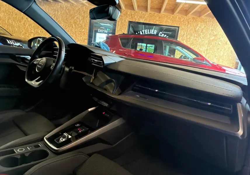 Vue intérieure côté conducteur de l’Audi A3 Sportback 2023 noire, avec tableau de bord moderne et volant multifonctions.