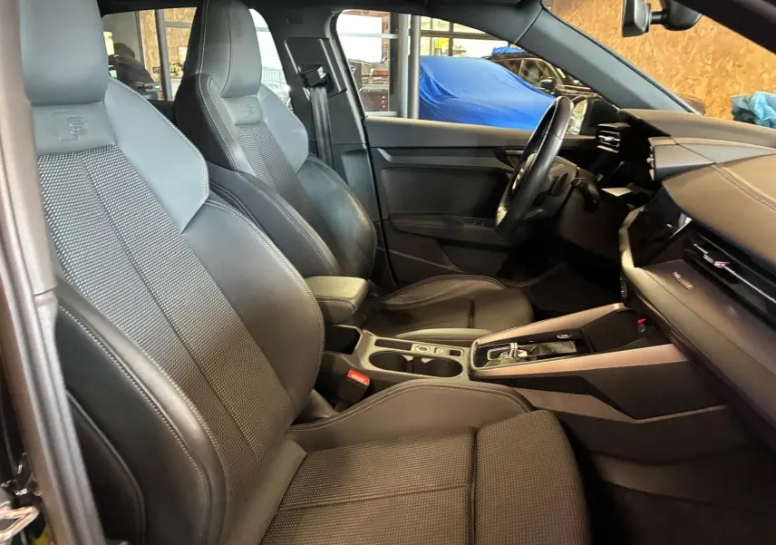 Vue intérieure côté conducteur de l'Audi A3 Sportback 2023, sièges sport noirs avec surpiqûres et volant multifonctions cuir.