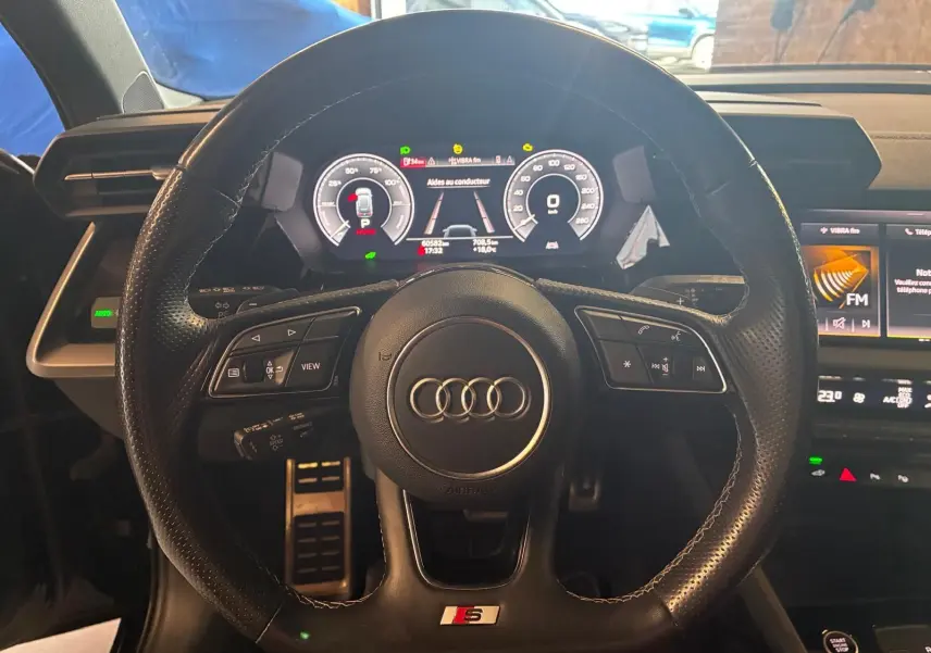 Vue centrée sur le volant cuir perforé S line de l'Audi A3 Sportback 2023 avec tableau de bord numérique allumé.