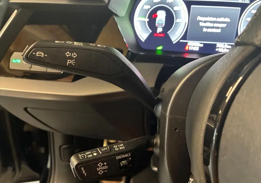 Gros plan sur les commandes au volant de l'Audi A3 Sportback 2023, affichage numérique et leviers noirs visibles.
