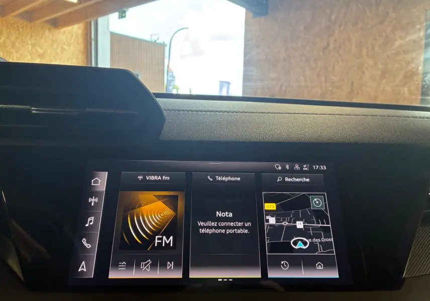 Écran central tactile de l’Audi A3 Sportback 2023 affichant radio FM, téléphone et navigation, vue intérieure frontale.