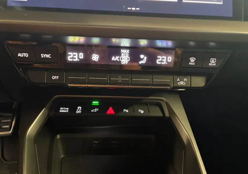 Vue rapprochée du tableau de bord noir de l'Audi A3 Sportback 2023, montrant la climatisation digitale et les commandes centrales.