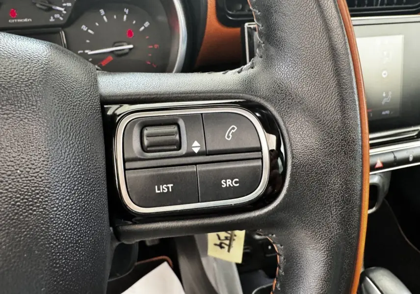 Gros plan sur le volant cuir noir du Citroën C3 Aircross 2020, avec commandes audio et écran tactile en arrière-plan.
