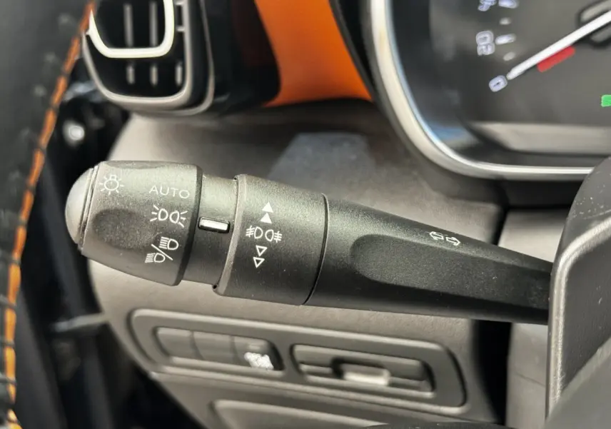 Gros plan sur la manette de commande des feux et clignotants du tableau de bord noir avec surpiqûres orange de la Citroën C3 Aircross.