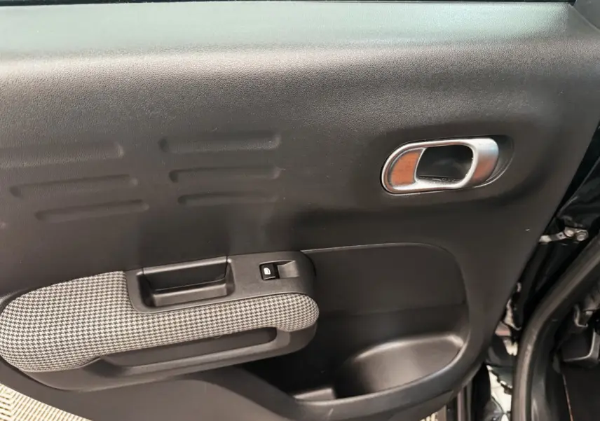 Gros plan sur la porte intérieure côté droit de la Citroën C3 Aircross noire, avec poignée chromée et accoudoir à motif pied-de-poule.