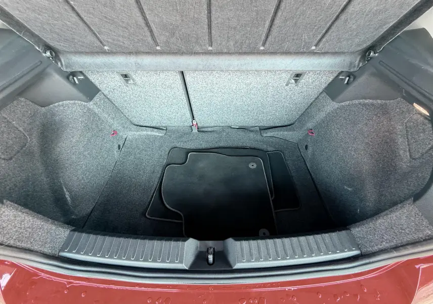 Vue plongeante sur le coffre vide d'une SEAT Ibiza rouge passion métal, avec tapis de sol noir à l'intérieur.