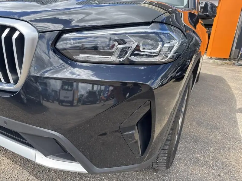 Gros plan sur l'avant droit d'une BMW X3 xDrive30e 2023 en Saphirschwarz métallisé, avec phares LED et calandre caractéristique.