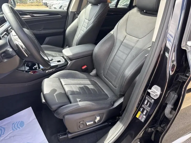 Vue intérieure côté conducteur du BMW X3 xDrive30e 2023 en Saphirschwarz, sièges sport cuir noirs avec réglages électriques.