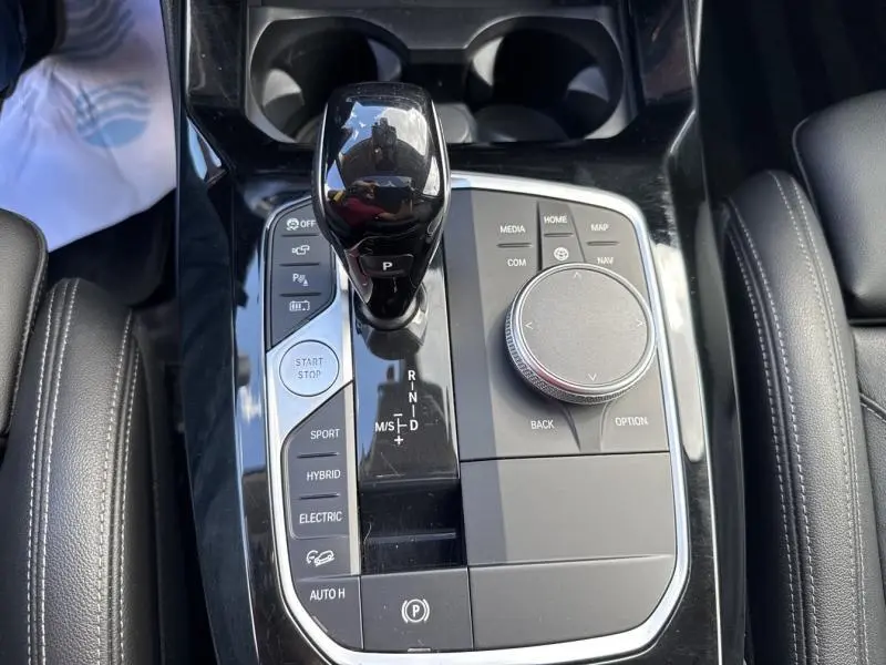 Vue plongeante sur la console centrale noire brillante du BMW X3 xDrive30e avec levier de vitesses et commandes multimédia.