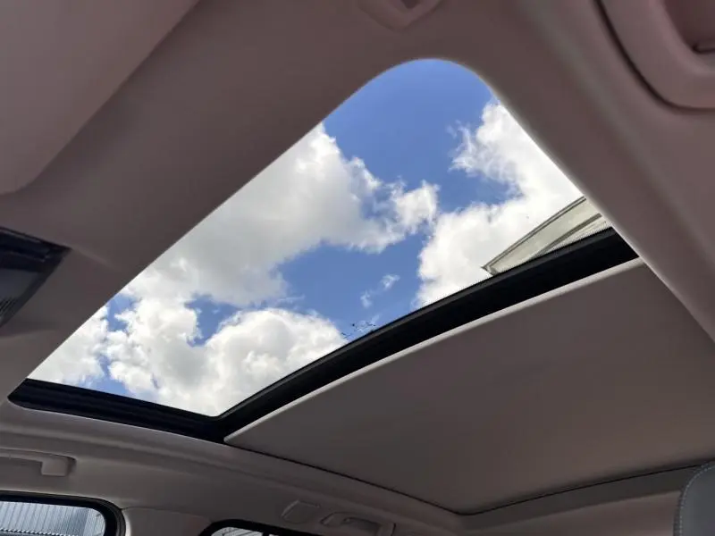 Toit ouvrant panoramique en verre ouvert sur ciel bleu, intérieur clair d’un BMW X3 xDrive30e Saphirschwarz métallisé.