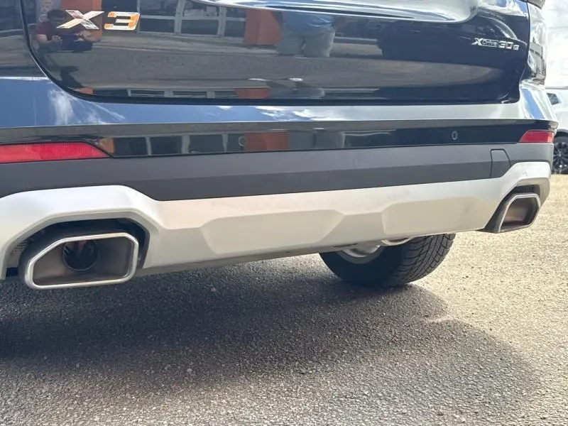 Vue rapprochée de l’arrière droit d’un BMW X3 xDrive30e 2023 noir métallisé avec double sortie d’échappement chromée.