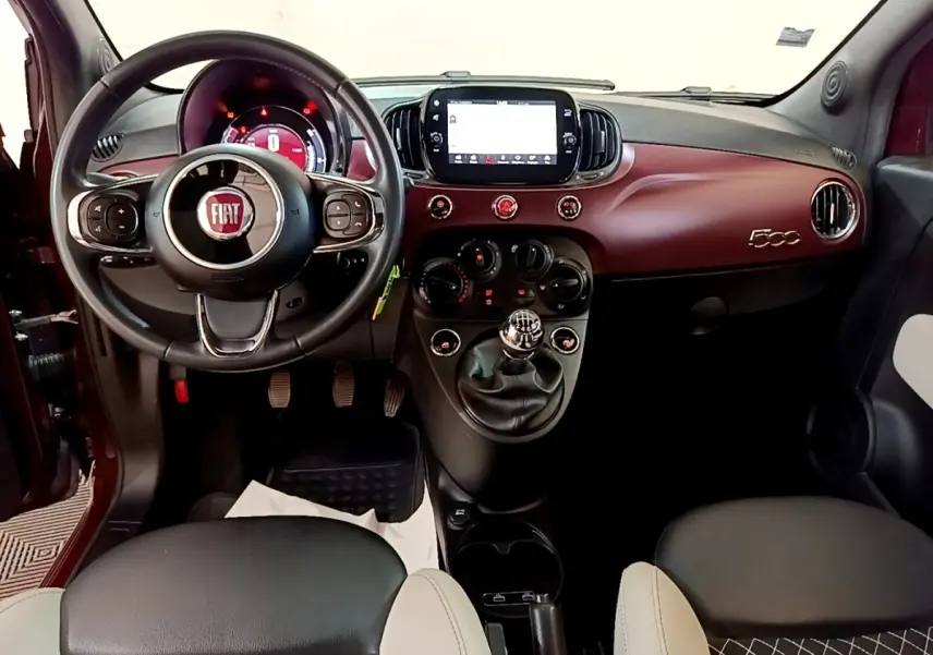 Vue intérieure avant de la Fiat 500 rouge, tableau de bord bordeaux avec écran tactile et volant cuir multifonctions.
