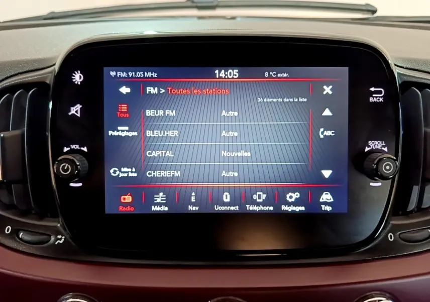 Écran tactile central de la FIAT 500 rouge de 2021 affichant la liste des stations radio FM.