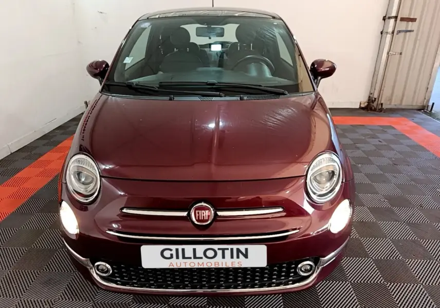 Vue avant d'une FIAT 500 rouge bordeaux avec phares allumés dans un garage intérieur.