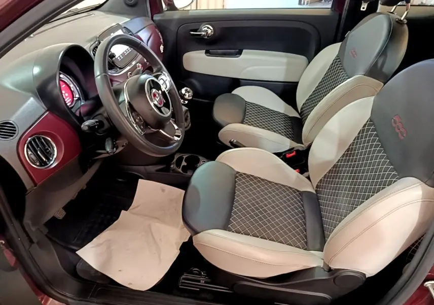 Intérieur côté conducteur de la Fiat 500 rouge 1.0 70ch BSG Star avec sièges bicolores et volant cuir multifonctions.