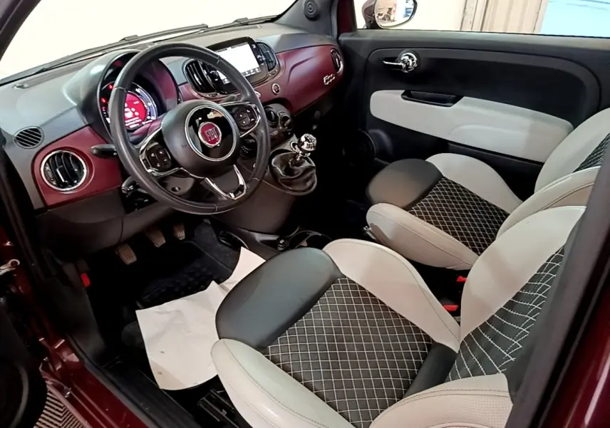 Intérieur côté conducteur de la Fiat 500 rouge, montrant tableau de bord bordeaux et sièges bi-ton noirs et blancs.