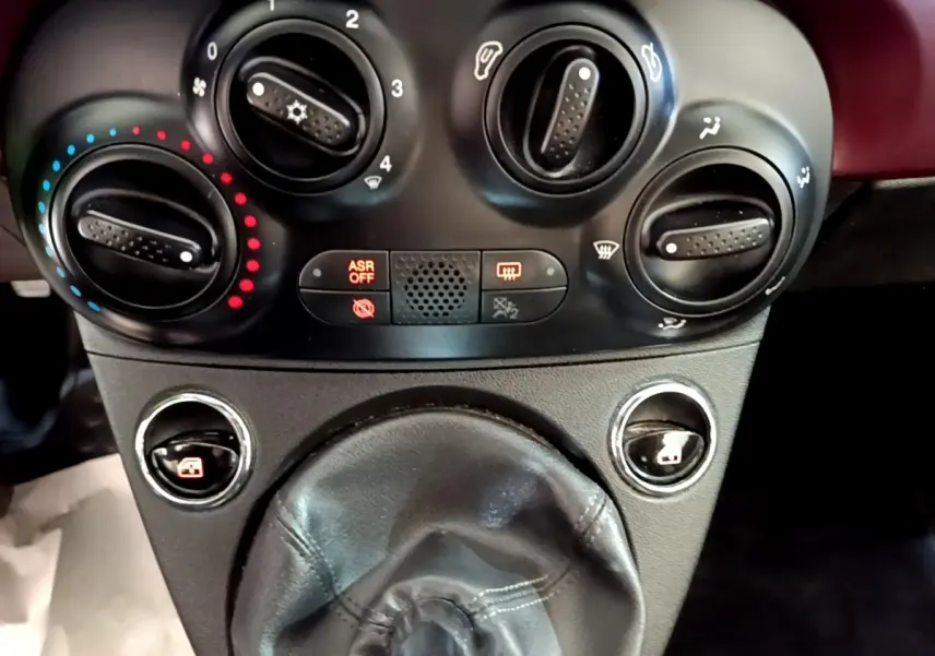 Gros plan sur les commandes de climatisation et la soufflet de levier de vitesse en cuir noir de la FIAT 500 rouge.