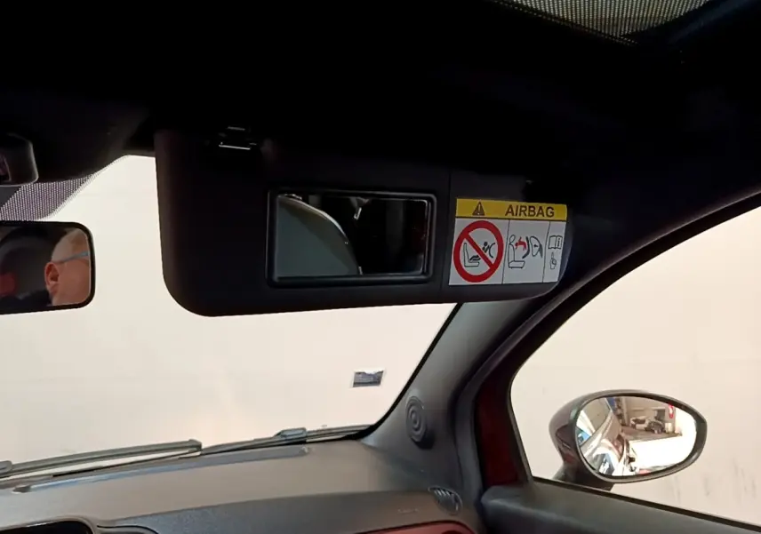 Détail intérieur montrant le pare-soleil avec miroir et avertissement airbag, côté conducteur d'une FIAT 500 rouge.