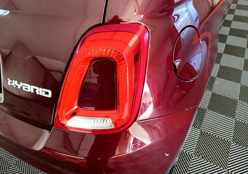 Gros plan sur le feu arrière droit rouge et l'inscription Hybrid d'une FIAT 500 rouge brillante.