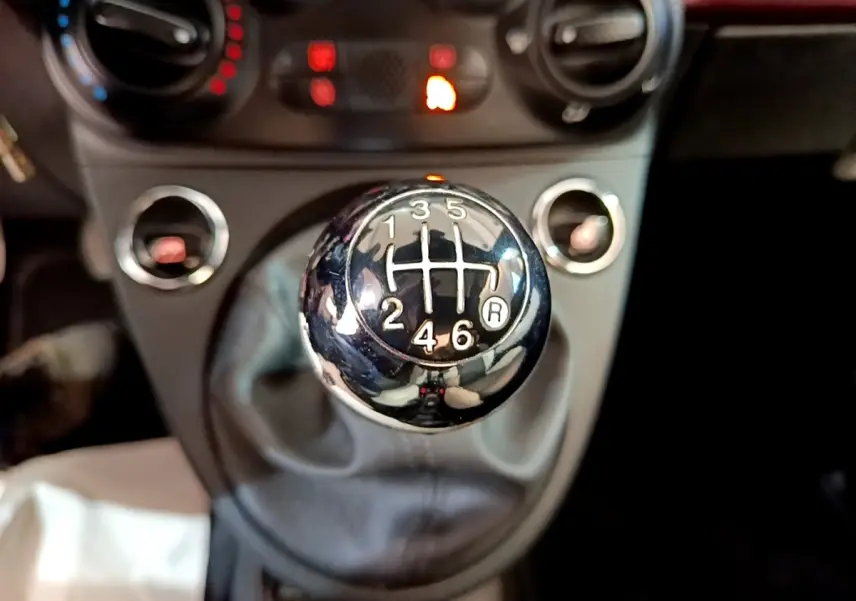 Gros plan sur le levier de vitesses manuel chromé de la FIAT 500 rouge, avec les commandes de climatisation en arrière-plan flou.