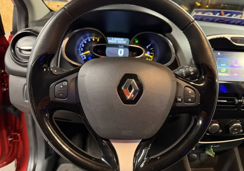 Vue rapprochée du volant noir de la Renault Clio Estate IV rouge, avec tableau de bord et écran tactile en arrière-plan.