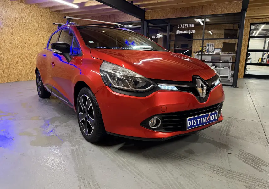 Renault Clio Estate IV rouge vue 3/4 avant droit avec barres de toit et jantes alliage noires.