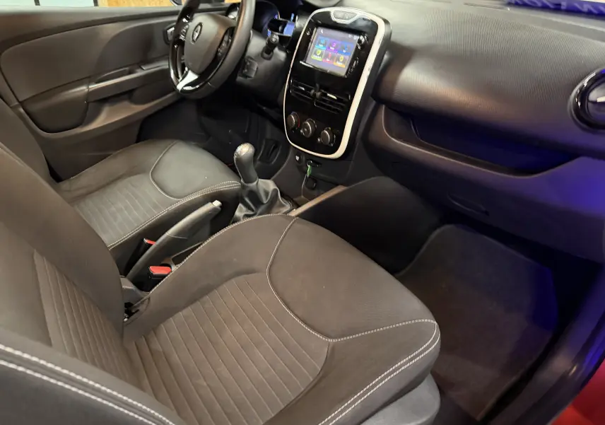 Vue intérieure côté conducteur de la Renault Clio Estate IV rouge, avec tableau de bord et console centrale tactile visible.