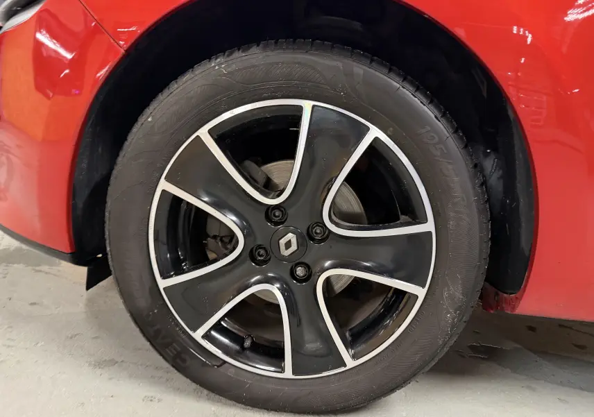 Gros plan sur la roue avant gauche d'une Renault Clio Estate IV rouge, avec jante noire et argentée design moderne.