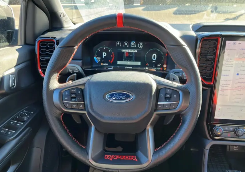Vue intérieure centrée sur le volant cuir noir avec surpiqûres rouges et logo Raptor rouge du Ford Ranger Raptor 2025.