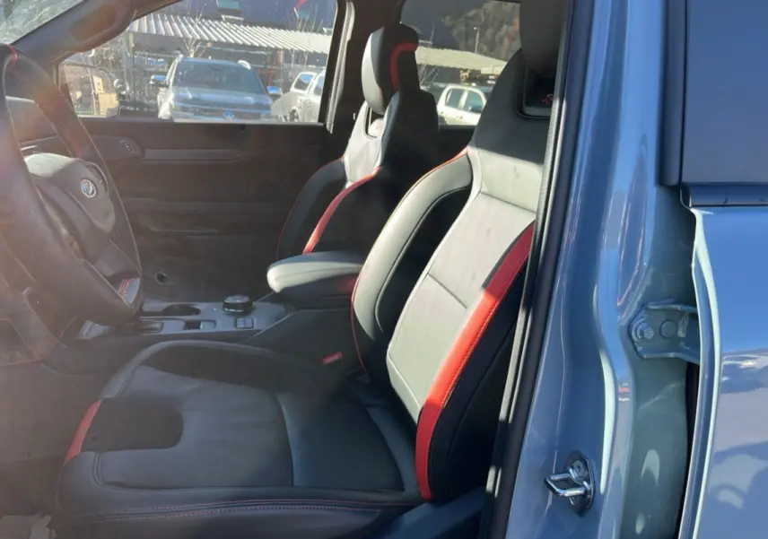 Vue intérieure côté conducteur du Ford Ranger Raptor 2025 gris commandeur, sièges sport cuir noir avec surpiqûres rouges.