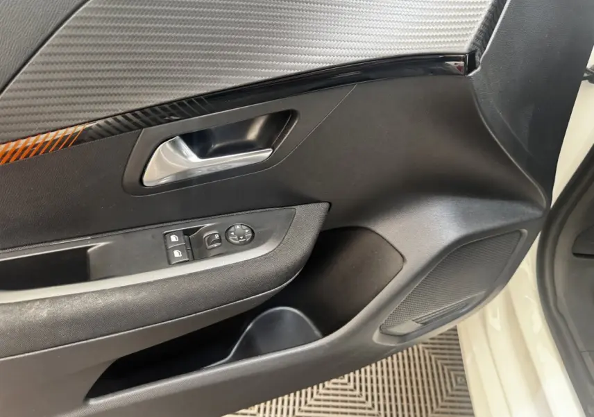 Vue intérieure côté conducteur de la porte noire avec poignée argentée et commandes électriques sur Peugeot 208 blanc.