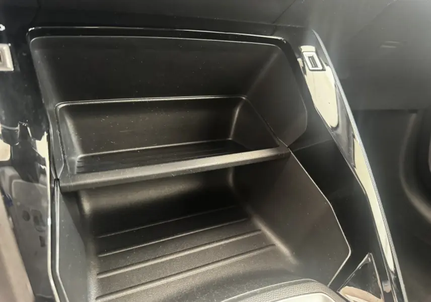 Gros plan sur le rangement intérieur noir du tableau de bord de la Peugeot 208 PureTech 100 blanche.