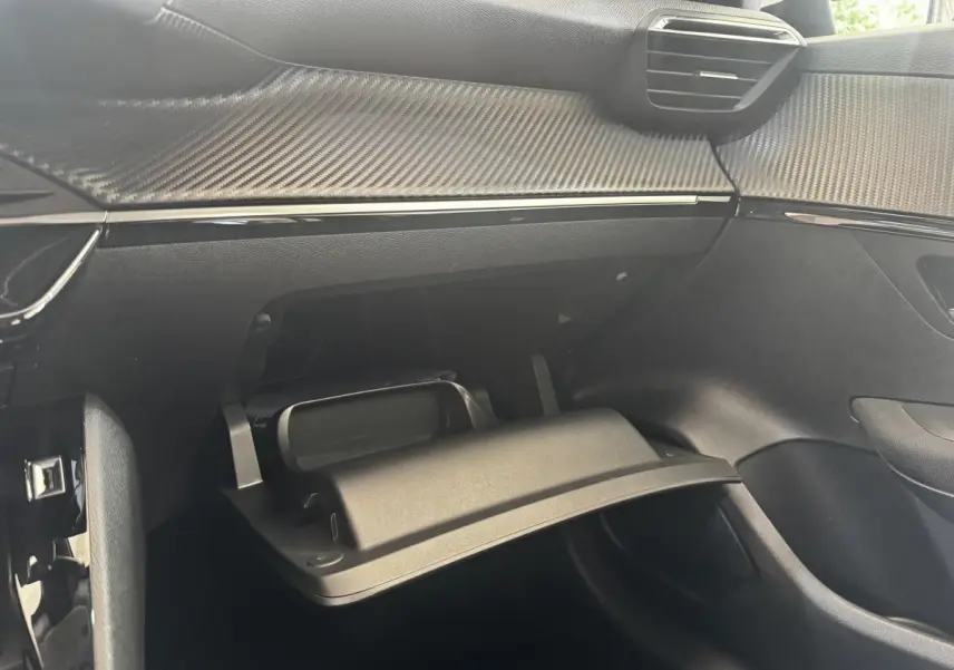 Vue intérieure côté passager de la Peugeot 208 2020, boîte à gants ouverte et tableau de bord noir avec insert effet carbone.