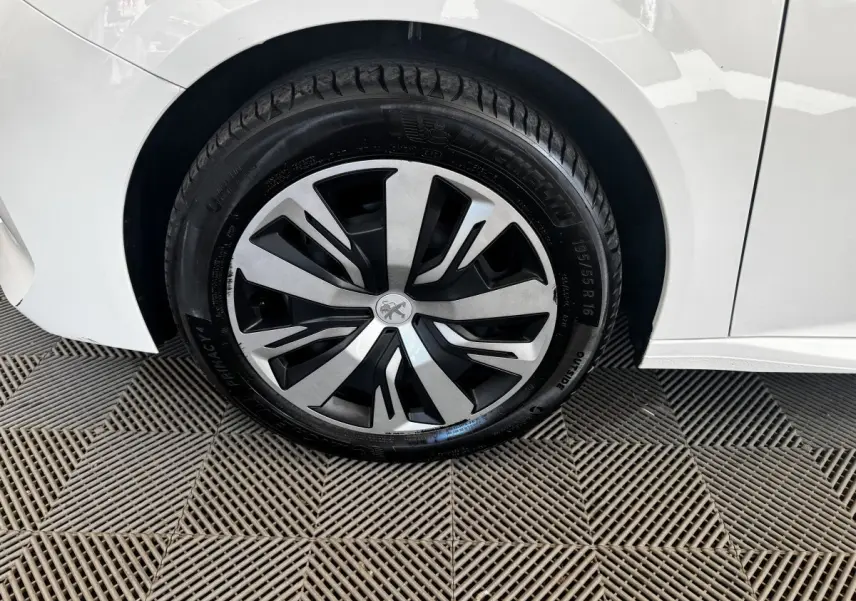 Gros plan sur la roue avant gauche d’une Peugeot 208 blanche avec jante alliage au design moderne.