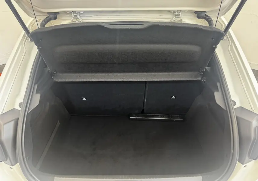 Coffre ouvert vu de l'arrière d'une Peugeot 208 blanche, montrant l'espace de chargement vide et la tablette de séparation.
