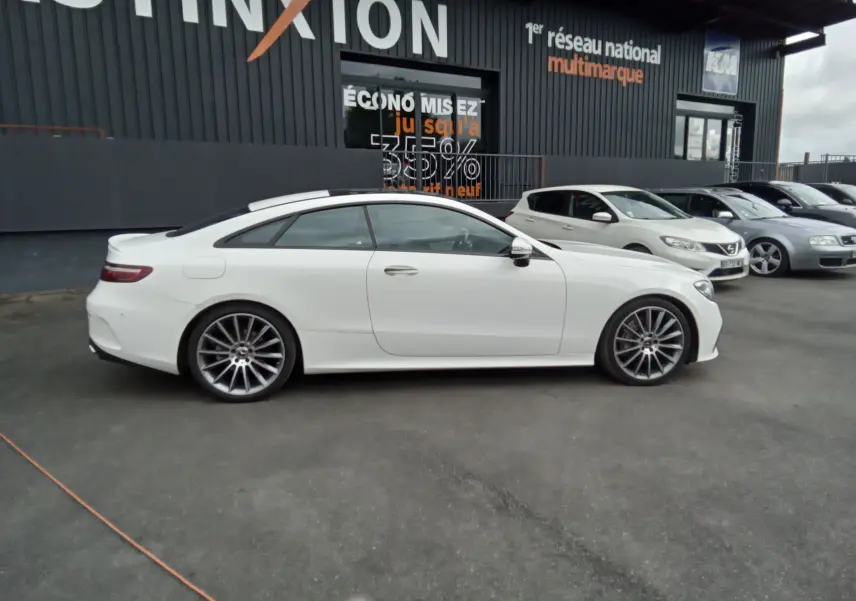 Mercedes Classe E Coupé 220D AMG Line blanc vu de profil côté gauche, avec jantes alliage et toit panoramique.