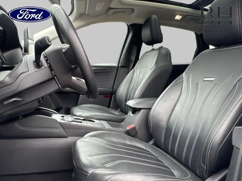 Vue intérieure avant du Ford Kuga 2022 avec sièges sport en cuir noir et toit panoramique visible au-dessus.