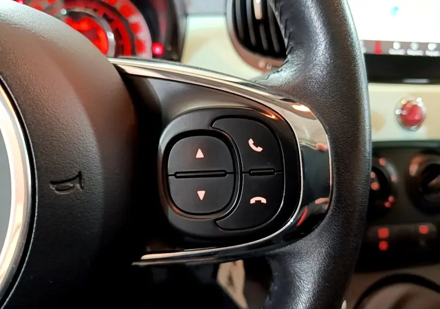 Gros plan sur les commandes du volant cuir noir de la Fiat 500 Lounge 2019, avec tableau de bord en arrière-plan.