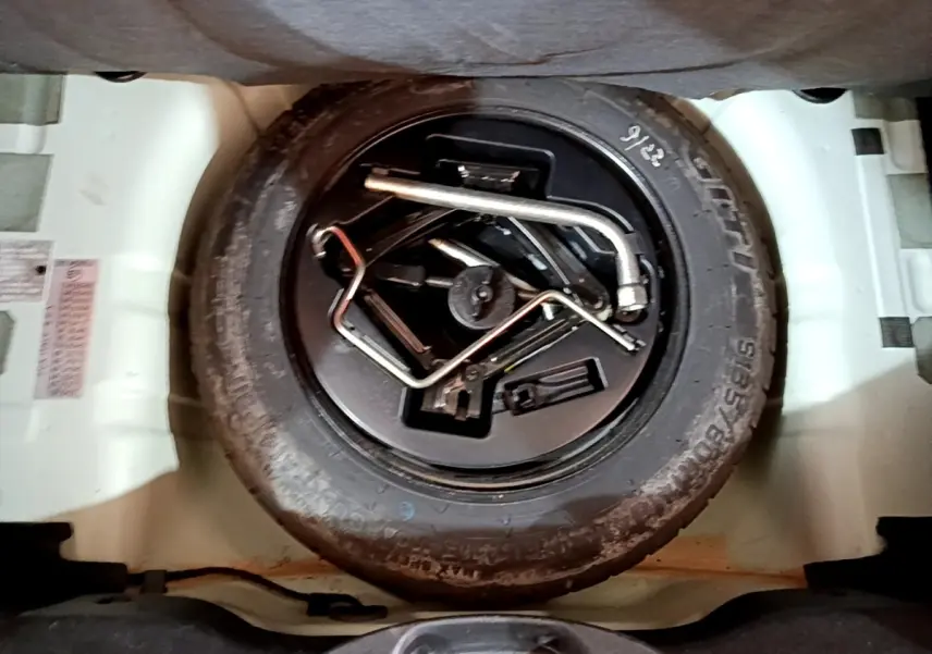 Roue de secours noire avec outils de changement dans le coffre d'une FIAT 500 verte, vue de dessus.