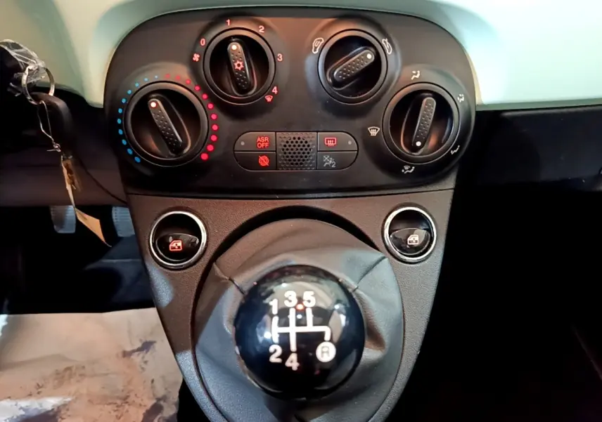 Gros plan sur la console centrale d'une FIAT 500 verte 2019, mettant en valeur le levier de vitesses manuel et les commandes de climatisation.