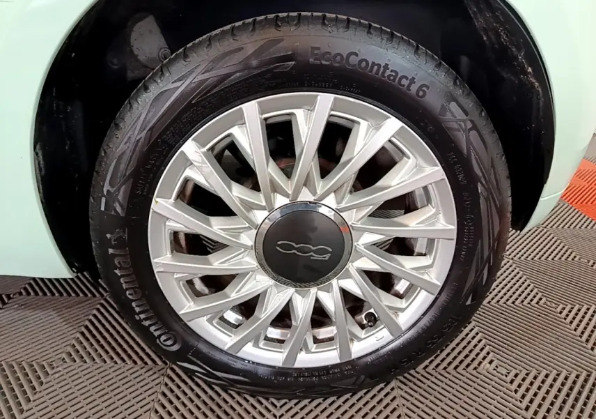 Gros plan sur la roue avant gauche d'une FIAT 500 verte, mettant en valeur la jante argentée au design étoilé.