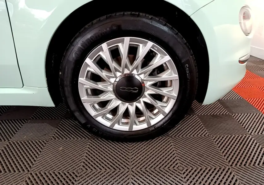 Gros plan sur la roue avant droite d'une FIAT 500 verte pastel, mettant en valeur la jante argentée au design fin.