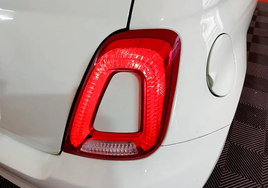 Gros plan sur le feu arrière droit rouge d'une FIAT 500 blanche, avec la trappe à carburant visible à côté.