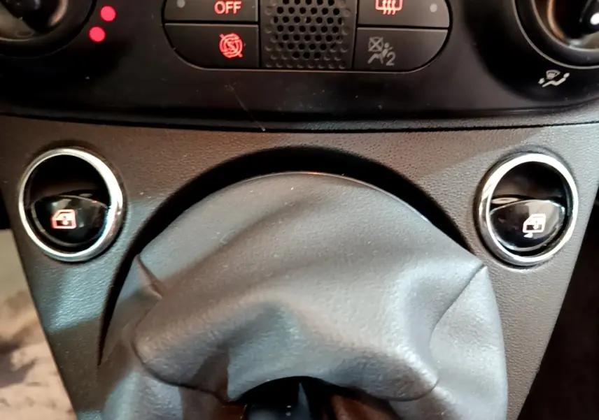 Gros plan sur la console centrale de la Fiat 500 Lounge 2019, montrant les commandes des vitres électriques et le soufflet de levier de vitesse noir.